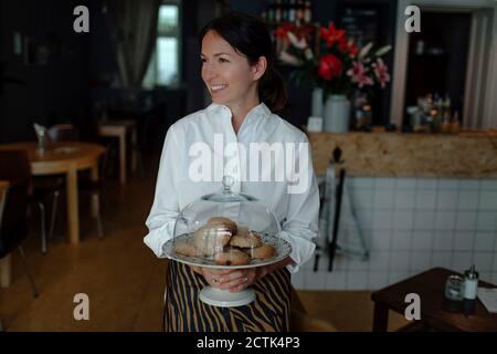 Sorridente proprietario femminile che tiene i biscotti nel piatto con chioche a. caffè Foto Stock