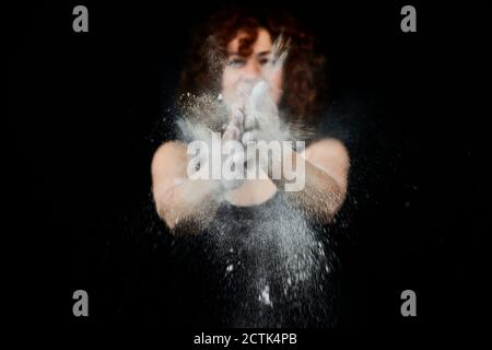Donna che batte le mani ricoperte di polvere bianca di fronte faccia su sfondo nero Foto Stock