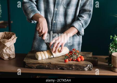 Metà dell'uomo che taglia il pane fresco fatto in casa con pomodori ciliegini a bordo in cucina Foto Stock