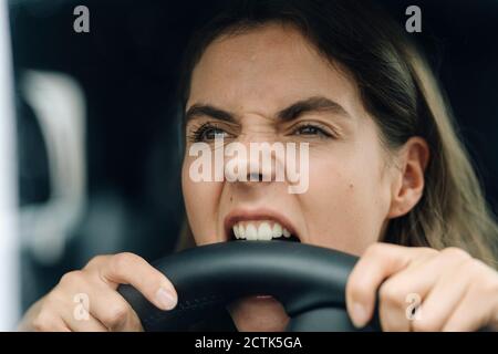 Primo piano di una donna arrabbiata che muta il volante mentre si è seduti in auto Foto Stock