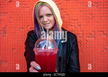 Ritratto di giovane donna con capelli tinti con bevanda da asporto davanti alla parete rossa Foto Stock