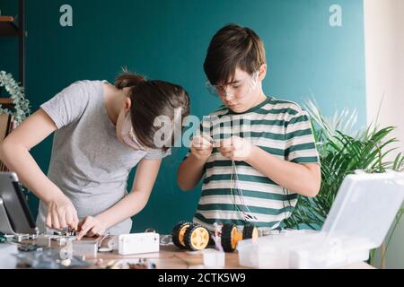 Fratelli che fanno giocattolo robotico sul tavolo a casa Foto Stock