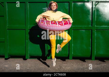 Giovane donna con capelli tinti e pneumatici galleggianti che danzano dentro parte anteriore del contenitore verde Foto Stock