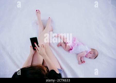 Madre che usa il telefono mentre si siede dalla bambina addormentata Foto Stock