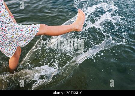 Ragazza che spruzzi d'acqua con le gambe in lago Foto Stock