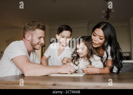 Sorridente genitori risolvere puzzle puzzle con bambini sul tavolo a. casa Foto Stock