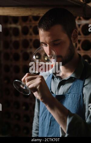 Giovane assaggiando il vino dal bicchiere in cantina Foto Stock