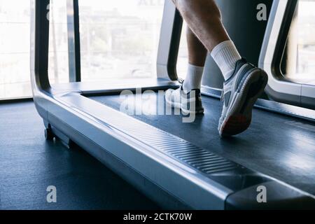 Gambe di atleta maschile che corre sul tapis roulant in palestra Foto Stock