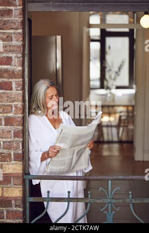 Donna che legge il giornale mentre in piedi in balcone Foto Stock