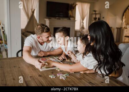 Sorridente genitori risolvere puzzle puzzle con bambini sopra tavolo a. casa Foto Stock