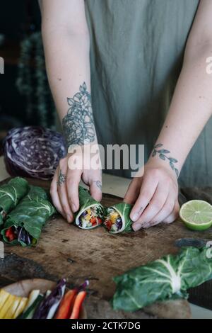 Giovane donna che prepara il rotolo vegano con le verdure sul tagliere Foto Stock