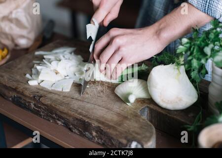 Mani di uomo che tagliano finocchio a bordo in cucina Foto Stock