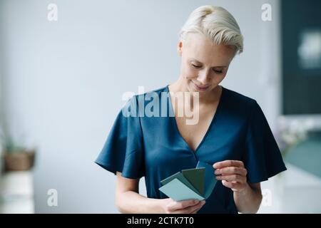 Primo piano di una donna d'affari che sceglie il campione di colore mentre si sta in piedi contro il muro in ufficio Foto Stock