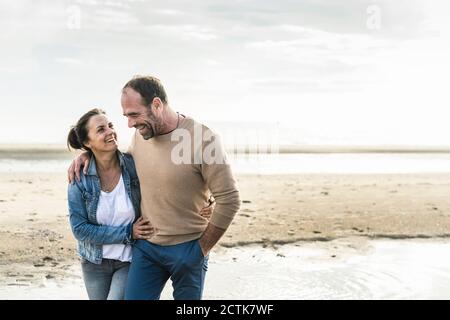Coppia matura allegra che si abbraccia mentre si levano in piedi contro il mare durante il fine settimana Foto Stock
