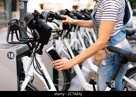 Sezione centrale della donna che esegue la scansione del codice QR sulla stazione di parcheggio per biciclette Foto Stock