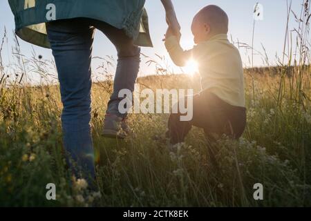 Ragazzo carino che tiene la mano della madre mentre cammina sul campo durante giorno di sole Foto Stock