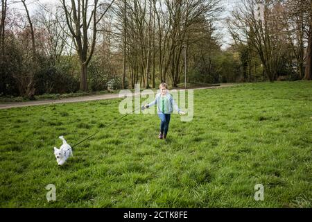 Ragazza sorridente che corre con il cane su erba in cortile Foto Stock