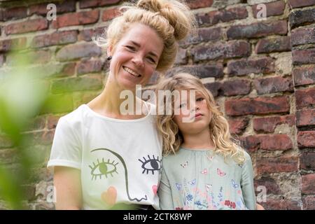 Donna bionda sorridente con figlia contro il muro di mattoni sul retro iarda Foto Stock