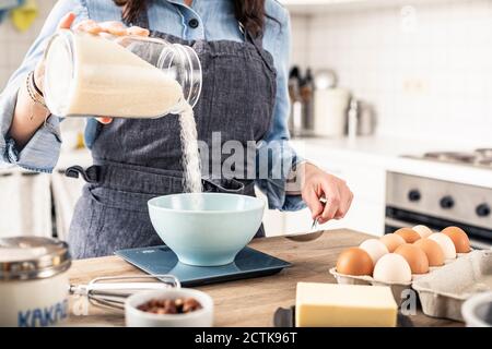 Donna che pesa la farina su scala di cucina per fare la torta a. casa Foto Stock