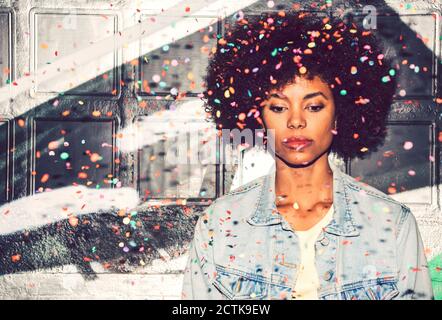 I confetti cadono sulla donna premurosa che guarda giù mentre si sta in piedi contro parete Foto Stock