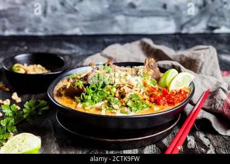Ciotola di zuppa di curry rosso con tagliatelle di riso, manzo, verdure, scalogno, arachidi e lime Foto Stock