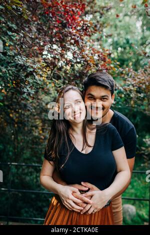 Un giovane sorridente che abbraccia la donna da dietro mentre trascorre il fine settimana al parco Foto Stock