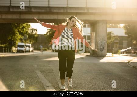 Giovane donna spensierata che corre con le braccia distese sulla strada Foto Stock