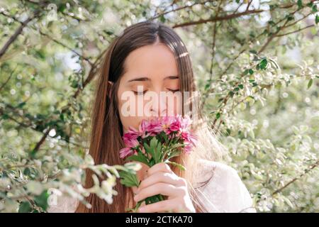 Donna che annuisce fiori rosa freschi mentre si trova in mezzo all'albero parcheggiare in primavera Foto Stock