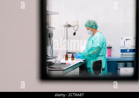 Donna scienziata che lavora al tavolo in laboratorio visto attraverso la finestra Foto Stock