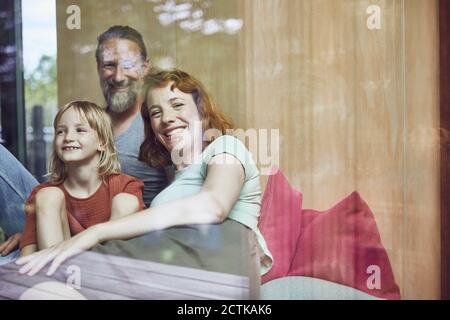 Sorridi i genitori con la figlia che si rilassa a letto a casa visto attraverso la finestra Foto Stock