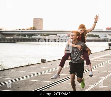 Uomo allegro che dà giro piggyback a donna al porto Foto Stock