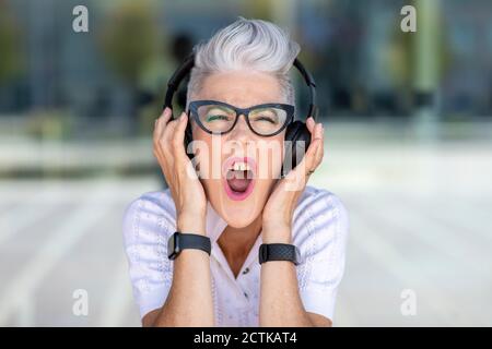 Una donna anziana entusiasta che urla mentre ascolti la musica tramite le cuffie Foto Stock