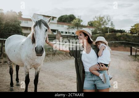 Madre che porta la figlia che accarezzava il cavallo mentre si trova sul sentiero Foto Stock