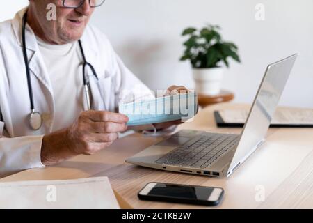 Medico che tiene la maschera chirurgica in clinica Foto Stock