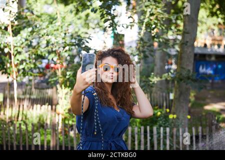 Giovane donna con occhiali da sole che prende un selfie con il suo smartphone in giardino Foto Stock