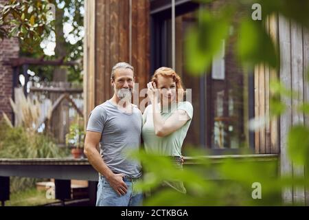 Coppia sorridente che si trova di fronte a una piccola casa in cortile Foto Stock