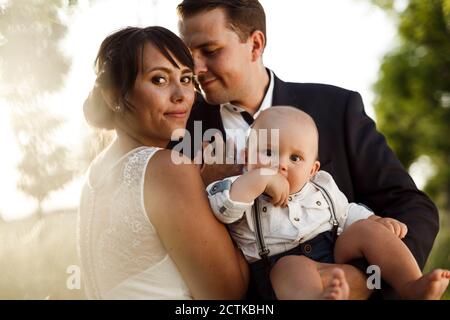 Bella sposa giovane con sposo e figlio al matrimonio durante tramonto Foto Stock