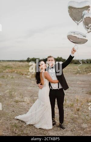 Sposa e sposo con palloncini a forma di cuore in piedi contro il cielo Foto Stock