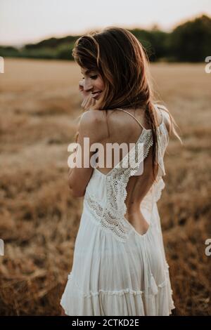 Donna che indossa un abito bianco che si affaccia sulla spalla mentre si sta in piedi campo di grano Foto Stock