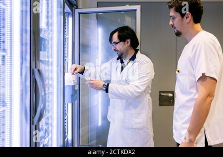 Farmacisti maschi che prendono inventario da frigorifero illuminato in ospedale Foto Stock