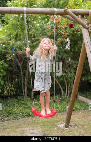 Bionda ragazza in piedi su swing a cortile posteriore Foto Stock