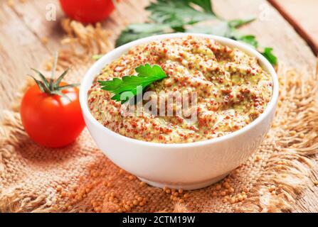 Senape francese fatta in casa con semi in ciotola bianca, salsa calda pronta, sfondo vecchio tavolo da cucina in legno, fuoco selettivo Foto Stock