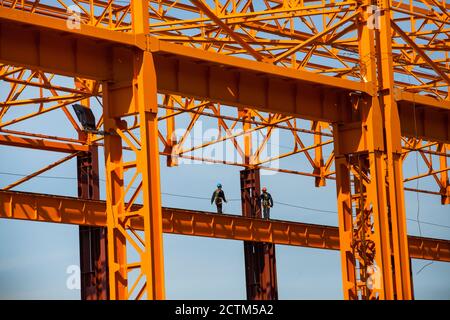 Kostanay/Kazakhstan - Maggio 14 2012: Costruzione di una nuova fabbrica. Assemblaggio di una struttura in acciaio arancione. Due lavoratori ad alta quota (o ind Foto Stock