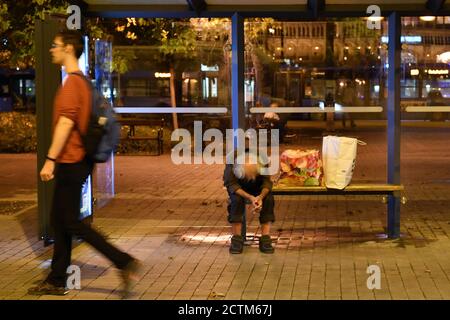 Budapest, Ungarn. 23 Settembre 2020. Un uomo senza casa si siede piegato in avanti ad una fermata dell'autobus - accanto a lui sono due borse di plastica - un passerby, un giovane uomo cammina oltre. Dopo, il 09/23/2020. | utilizzo in tutto il mondo credito: dpa/Alamy Live News Foto Stock