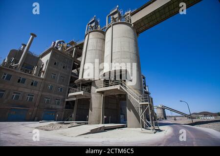 Moderna pianta di cemento nel deserto. Silos di cemento (torre di cemento), costruzione di fabbrica e trasportatore su cielo blu. Foto Stock