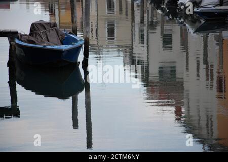 barca blu ormeggiata e riflessi d'acqua delle case colorate Lungo il canale nel comune di Chioggia nel Laguna Veneziana Foto Stock