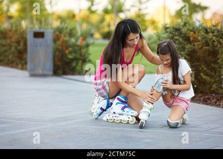 la bambina è caduta giù mentre rotola con la madre nel parco. mamma aiuta la figlia a alzarsi dopo la caduta Foto Stock