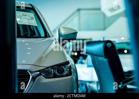 Fuoco selettivo sul faro di auto bianca lucente parcheggiata nello showroom. Vista frontale della nuova auto in showroom moderno in vendita. Concetto di concessionario auto. Elettrico Foto Stock