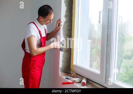 l'operatore in uniforme installa un pannello sandwich di plastica sul pendenze della finestra Foto Stock