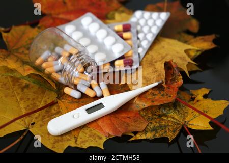 Termometro e pillole su foglie di acero giallo e rosso, flacone di capsule e blister confezione di compresse. Concetto di antipiretico, vitamine per l'immunità Foto Stock